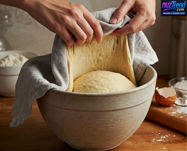 Pizza dough rising in a bowl covered with plastic wrap